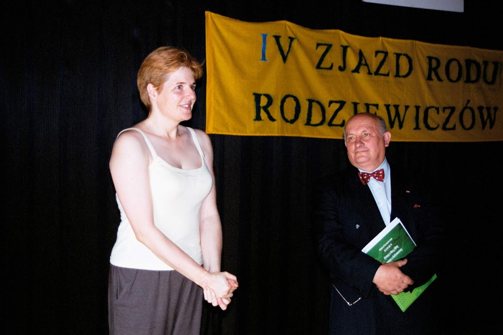 Dwie osoby na scenie podczas IV Zjazdu Rodu Rodziewiczów, z banerem w tle