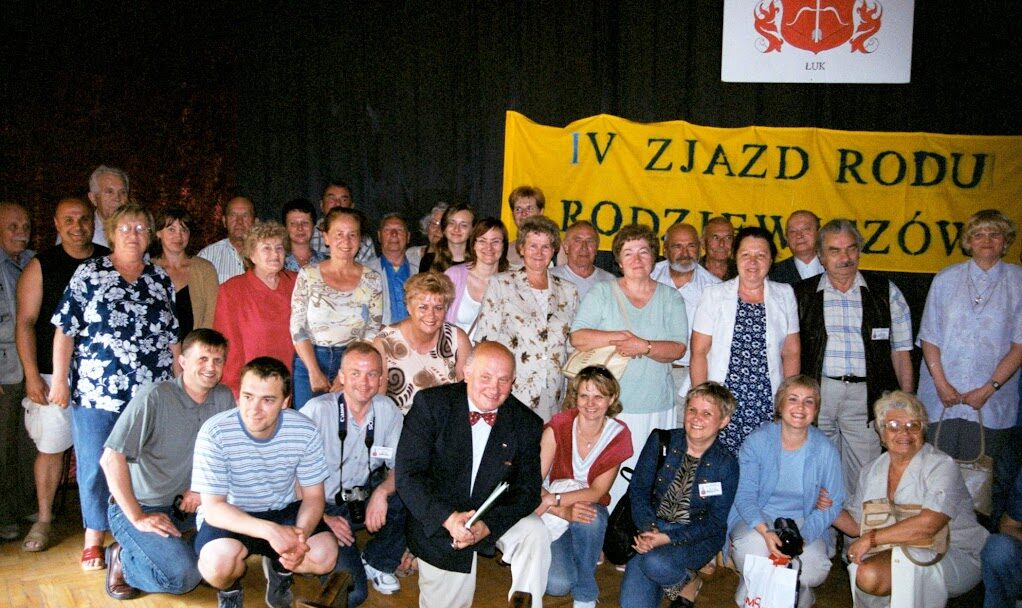 Grupowe zdjęcie uczestników V Zjazdu Rodu Rodziewiczów, Międzywodzie 2006, wykonane w sali z banerem i godłem